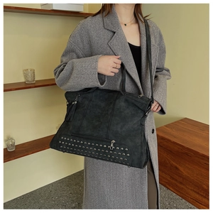 Detail of a black large capacity tote bag with rivet studs and tassel on a gray coat