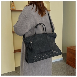 Detail of dark grey suede tote bag with metal studs and tassel shown on a model