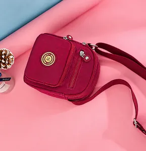 Macro view of burgundy oxford nylon crossbody bag with multiple zip compartments and logo