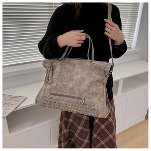 Detail of grey vintage tote bag with metal studs, fringe tassel and removable strap