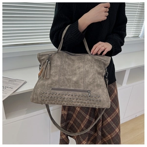 Detail of vintage grey leather tote featuring metal rivets, tassel, and zipper pocket