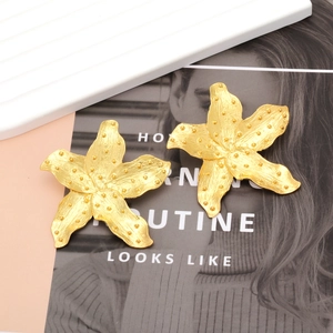 Golden alloy flower earrings with brushed texture on a fashion magazine background