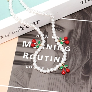 Elegant beaded pearl necklace with red cherry pendants on a soft aesthetic background