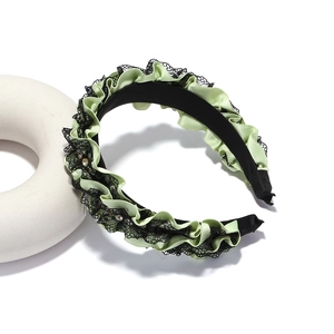 Detail of light green pleated satin headband with black lace trim and sparkling rhinestones