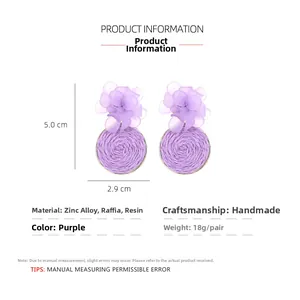 Detail of handmade purple resin flower earrings with raffia woven drops and metal core
