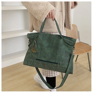 Detail of vintage green tote bag featuring metallic rivets, tassels and matte texture