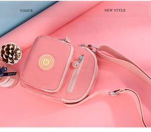 Pink nylon crossbody bag detail showing multi-layered zippers and brand logo patch