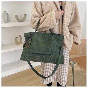 Detail of dark green vintage tote bag with retro rivets, fringe tassel and wide strap