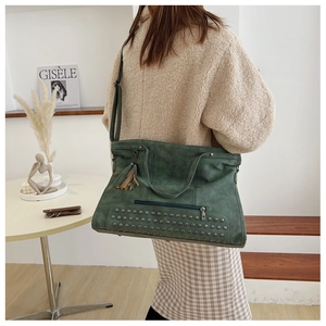 Detail of dark green tote bag with vintage rivets, leather tassels, and front zipper pocket
