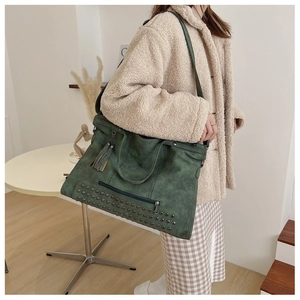 Detail of dark green vintage tote bag featuring decorative rivets and tassel charm