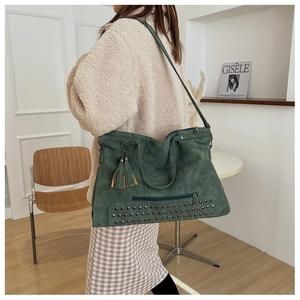 Detail of dark green suede tote bag with vintage rivets and tassel charm on a model