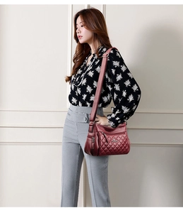 Detail of burgundy quilted crossbody bag with metal kangaroo logo and adjustable strap