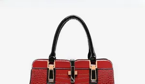Gros plan du sac à main rouge texture crocodile avec poignées noires et détails dorés