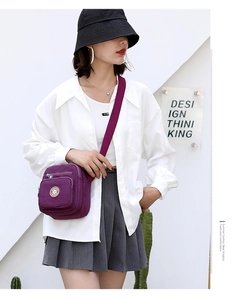 Detail of purple nylon crossbody bag featuring multi-zipper layers and adjustable strap
