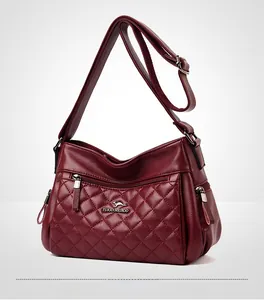Detail of burgundy quilted crossbody bag with metal logo and textured diamond stitching