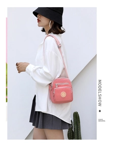 Pink nylon crossbody bag shown on a model with adjustable strap and multiple zipper pockets
