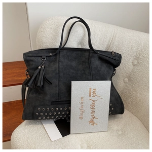 Detailed close-up of a black oversized tote with silver rivets and leather tassel accents
