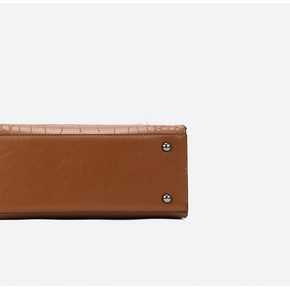 Detail van krokodillenreliëf leren handtas met zilveren metalen voetjes aan de basis
