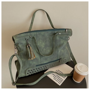Detail of dark green matte leather tote bag with silver studs and tassel ornament