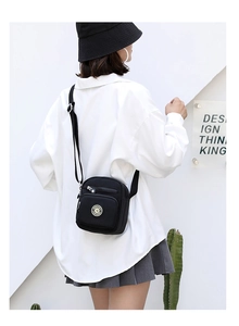 Outdoor shot of a black Oxford cloth crossbody bag with multiple zip compartments and logo