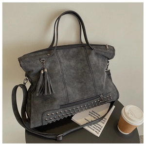 Macro detail of dark grey tote bag featuring metal rivets and long fringe tassels