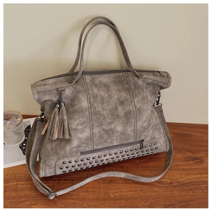 Detail of grey vintage tote bag showing rivet accents, fringe tassel, and leather texture