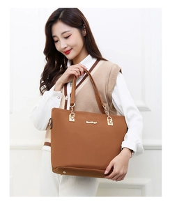 Brown tote bag with adjustable strap and metal chain detail shown on a model