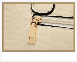 Vue macro du cuir crème à motif crocodile et des finitions de la fermeture éclair dorée