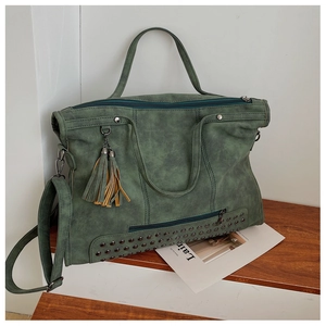 Close-up of vintage green tote with metal studs and tassel details on a wooden bench