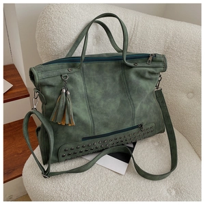 Macro detail of green retro leather tote featuring metal rivets and tassels on white sofa