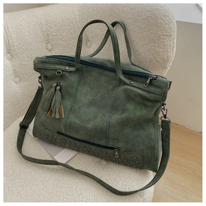Detail of dark green tote bag with tassels and rivets on a soft white sofa surface