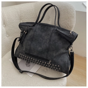 Detail of grey studded tote bag with fringe and zippers on a soft white sofa