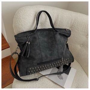 Detail of dark grey tote bag with rivets and tassels on a cozy white chair