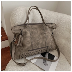 Detail view of vintage grey tote bag with tassel charm, metal rivets and matte texture