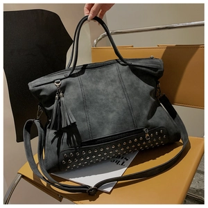 Detail of dark grey tote bag with metallic studs, leather fringe, and dual handles