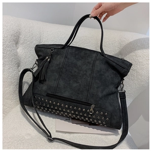Detail of black rivet tote bag with fringe tassels on a soft white sofa background