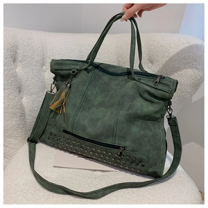 Detail of dark green vintage tote bag with rivet base and tassel charm on white fleece