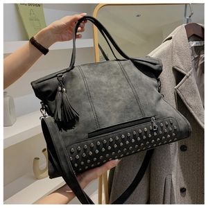 Detail of grey suede tote bag featuring metallic studs, fringe charms and dual straps