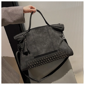Detail of dark gray tote bag featuring decorative metal studs and fringe tassel accent