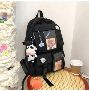Détail d'un sac à dos noir avec un pendentif vache en peluche et des badges de dessin animé