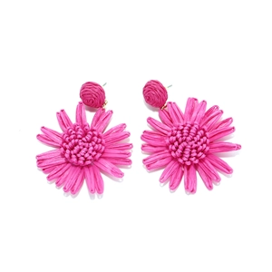 Détail de boucles d'oreilles tournesol en raphia fuchsia faites à la main avec pétales tressés