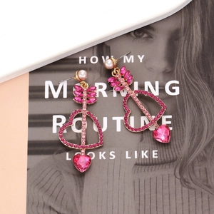 Détail de boucles d'oreilles cœur en cristal rose avec flèche de Cupidon et perles