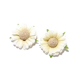 Detail of two handmade white fabric daisy earrings with woven centers and green leaves