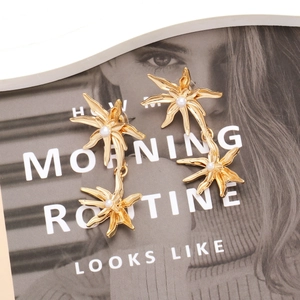 Gold flower earrings with pearls shown on a fashion magazine background with artistic layout