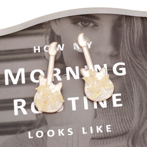 Detail shot of cream guitar stud earrings with golden butterfly accents and enamel finish