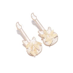 Detailed macro view of white guitar-shaped earrings with gold trim and butterfly accents