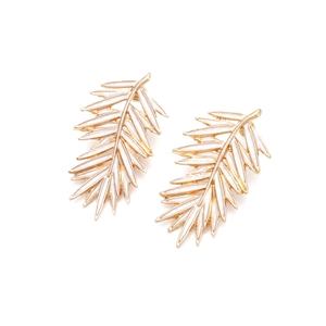 Détails macro des boucles d'oreilles feuilles aux contours dorés et émail blanc