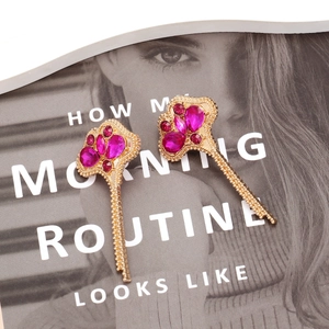 Elegant gold leaf earrings featuring vibrant pink rhinestones on a fashion magazine background