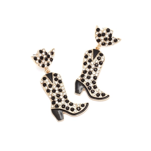 Gros plan de boucles d'oreilles bottes de cowboy dorées avec strass noirs et blancs