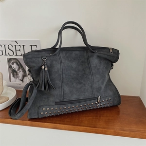 Vintage studded tote bag with tassels and adjustable strap on a minimalist wooden shelf